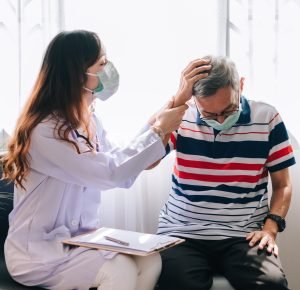 Asian doctor visit and examines a senior man at home with headage pain. The doctor checking up and consulting for retirement health ,hospital services ,and wearing a mask to protect covid-19.